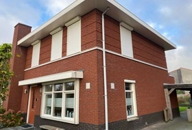 Klassieke rode bakstenen woning met witte rolluiken aan de voorzijde