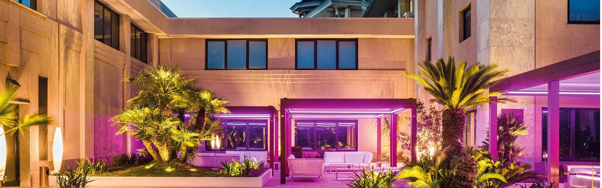 Hotelterras onder een lamellenoverkapping verlicht in paarse tinten