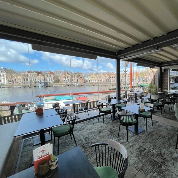 Overkapping bij barcafé met doorzichtige glazen wanden en terras aan het water
