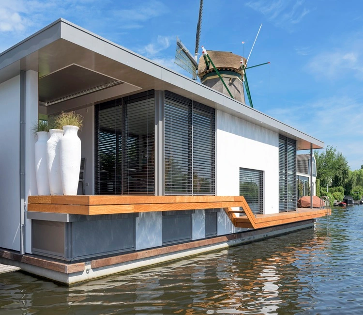 Woonboot met strak design aan het water, met een windmolen op de achtergrond