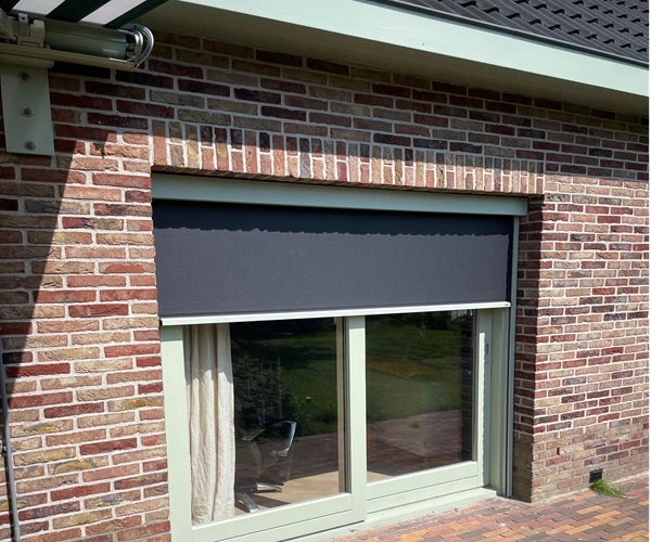 Zipscreen in antraciet kleur geïnstalleerd voor een raam van een huis met bakstenen muur.