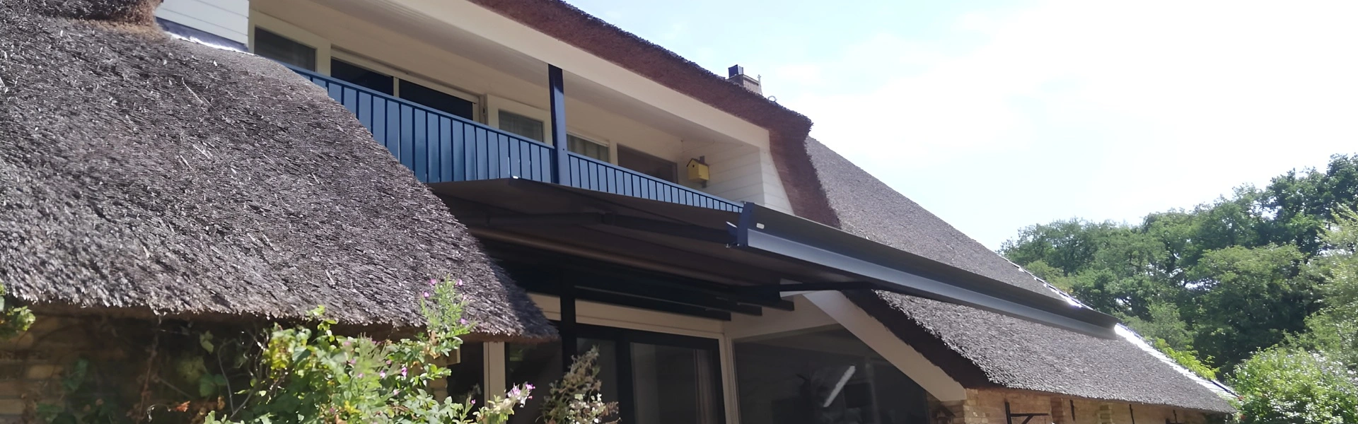 Huis met rieten dak en zon- en regenwerende schermen, omgeven door bomen