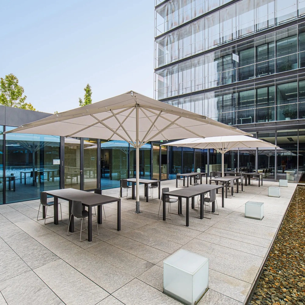 Parasol Albatros bij een kantoorgebouw met terrastafels en stoelen op een betegeld terras