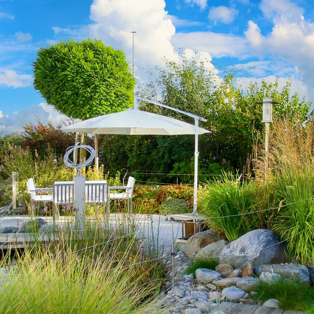 Parasol Rialto boven witte loungeset bij een groene tuin