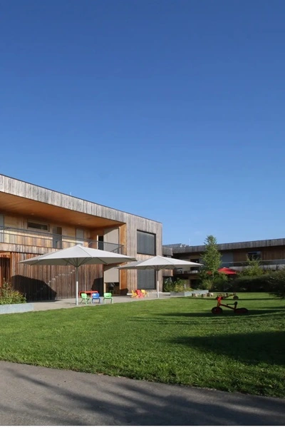 Parasol Schatello bij kinderopvang met houten gebouw en groene grasveld Parasol Schatello bij kinderopvang met houten gebouw en groene grasveld