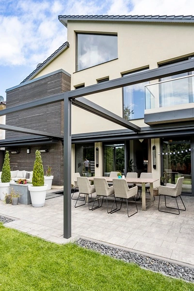 Pergola Sunrain Q over terras bij grote woning met eettafel en stoelen Pergola Sunrain Q over terras bij grote woning met eettafel en stoelen