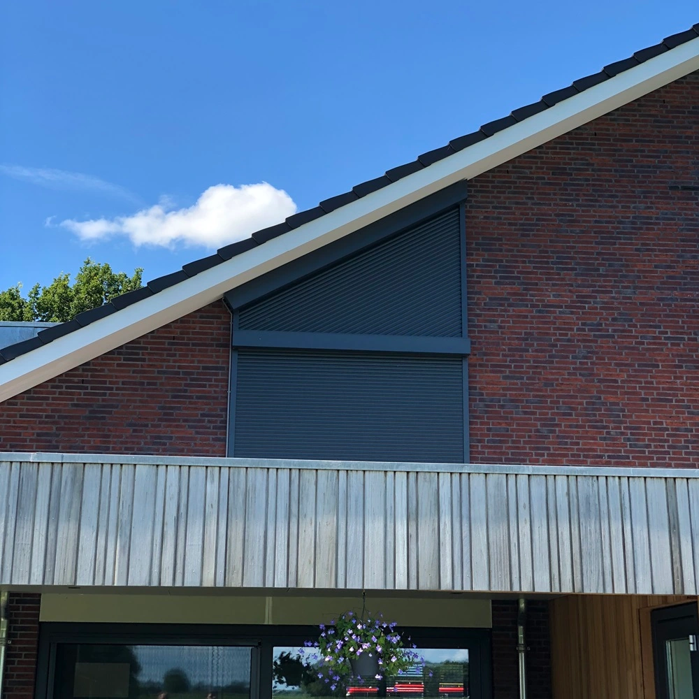 Gesloten Roma rolluik op een schuin dak van een huis met bakstenen gevel en houten balkon