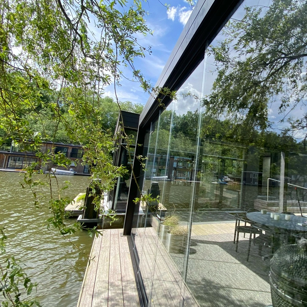 Glisse glazenschuifwand naast water met reflectie van de omgeving in het glas