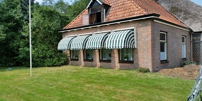 Groen-wit gestreepte markiezen op rij voor ramen van bakstenen huis met rood dak Groen-wit gestreepte markiezen op rij voor ramen van bakstenen huis met rood dak