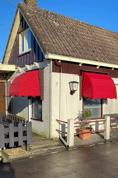 Horeca markies in felrode kleur boven raam van restaurant met witte gevel Horeca markies in felrode kleur boven raam van restaurant met witte gevel