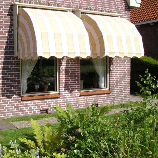 Houten markies in beige-witte strepen boven twee ramen van een bakstenen huis met tuin