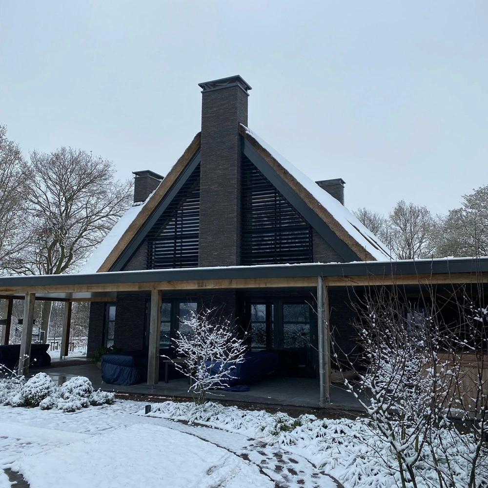 Louvre zonwering op gevel van huis met rieten dak en sneeuw in de tuin
