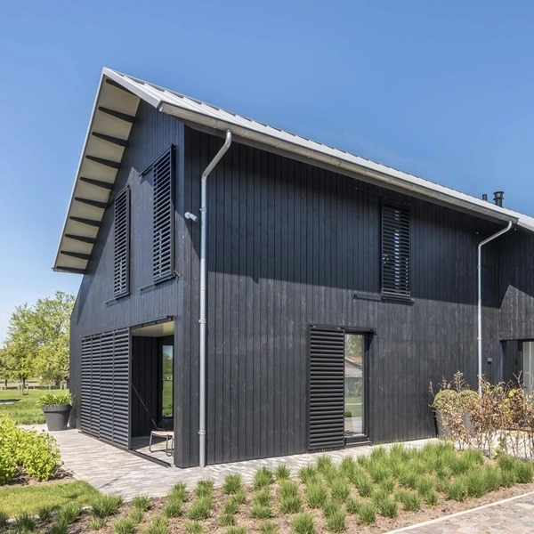 Schuifluiken op een zwart houten huis met lichte dakrand en groene tuin