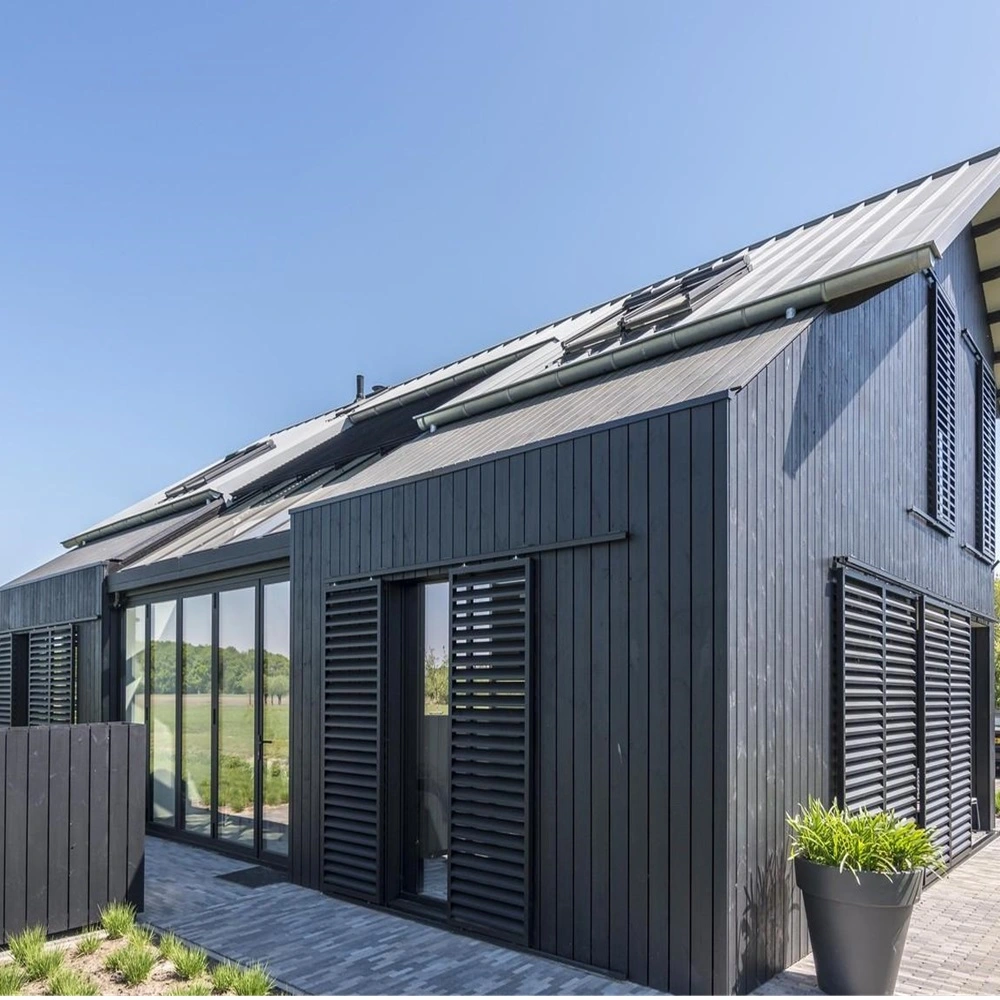 Schuifluiken op zwart houten huis met glazen schuifpui en zicht op groene velden