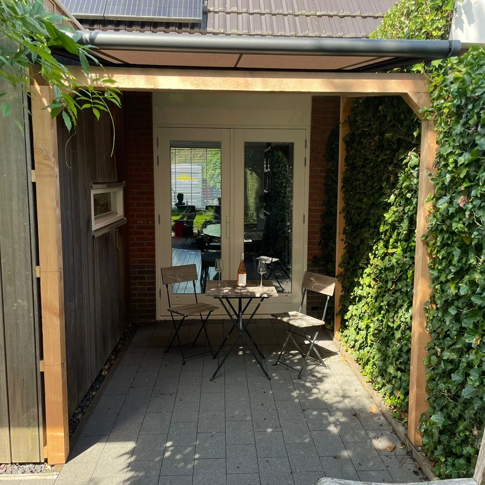 WGM TOP Serrezonwering boven een zithoek op een betegeld terras omgeven door houten panelen