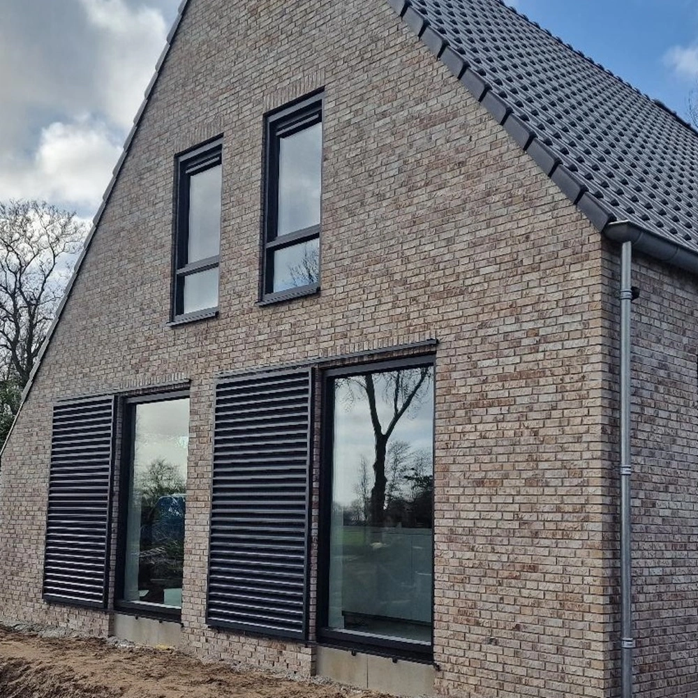 Zicht op schuifluiken op een bakstenen huis met grote ramen