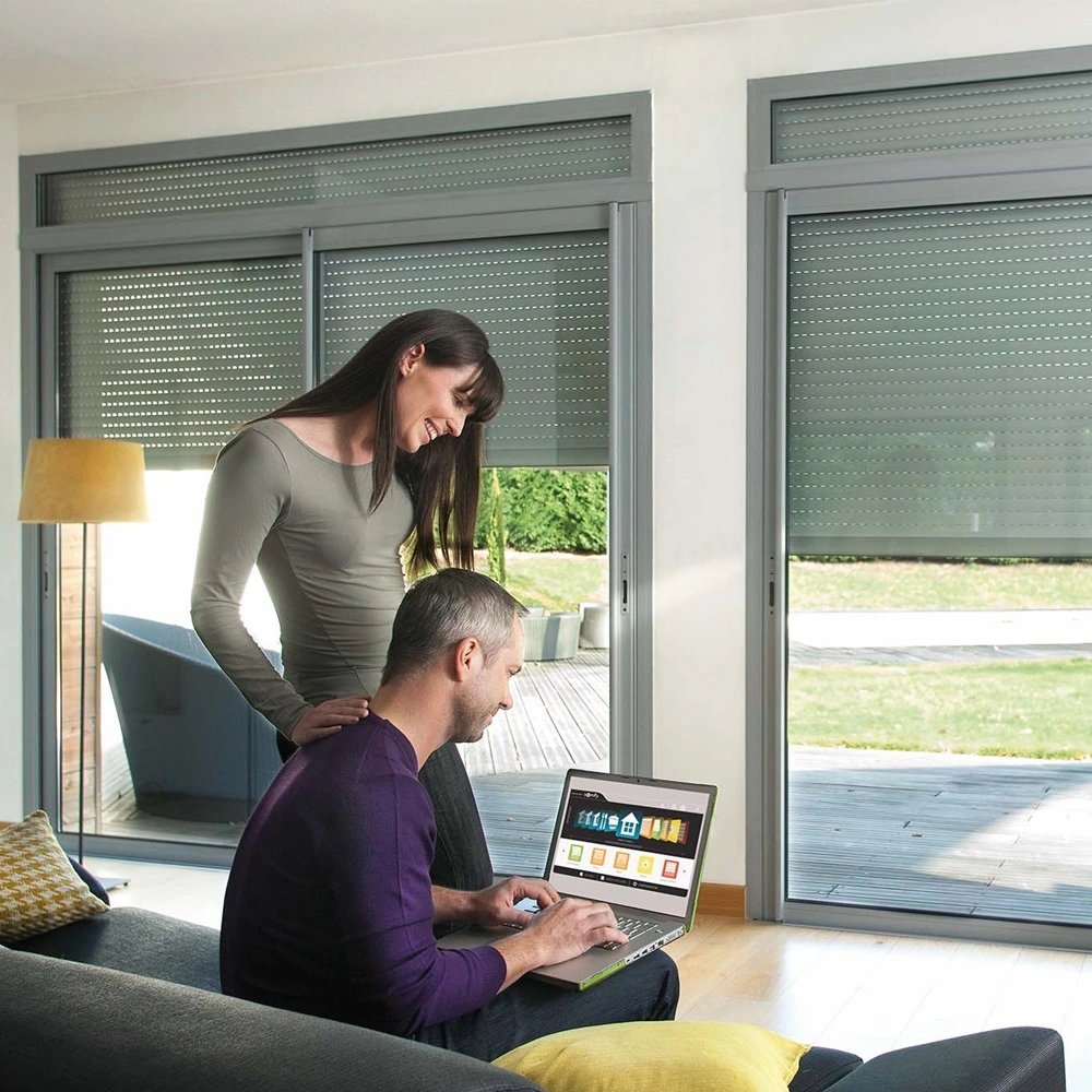 Man bedient zonwering via laptop, vrouw kijkt mee in de woonkamer