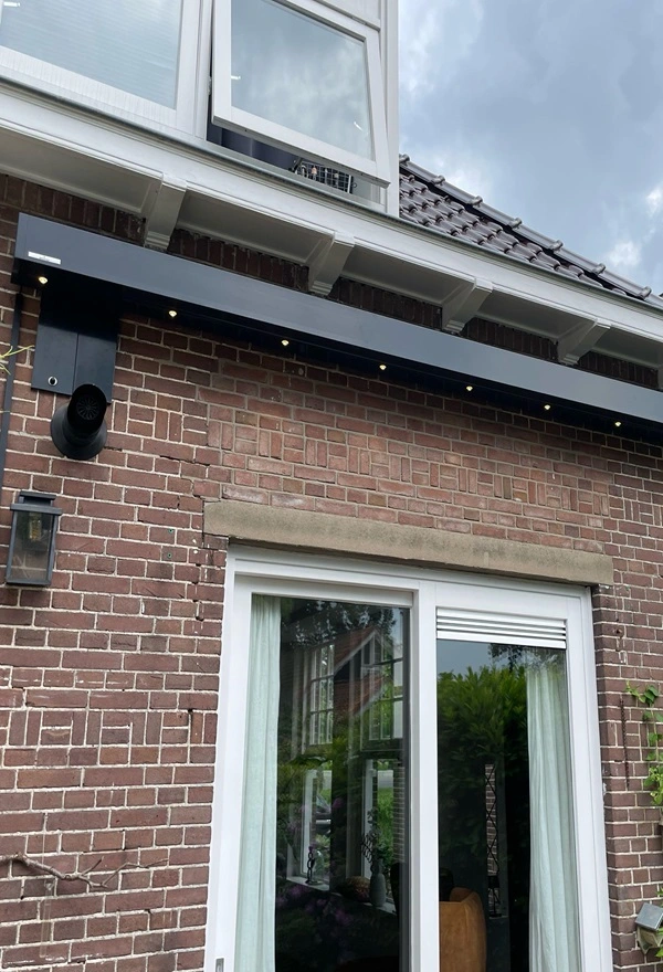Knikarmscherm aan gemetselde muur boven schuifdeuren met verlichting Knikarmscherm aan gemetselde muur boven schuifdeuren met verlichting