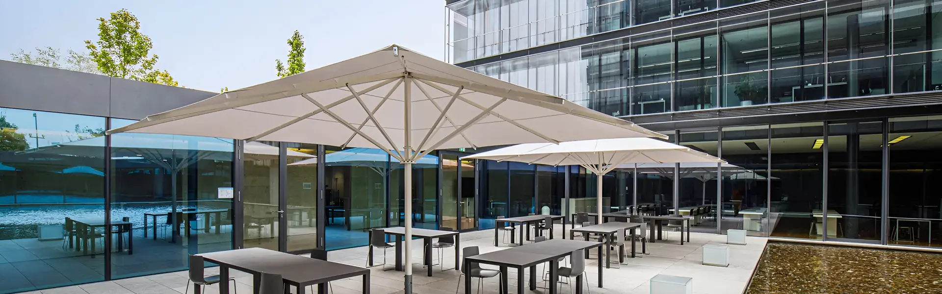 Luxe terrasopstelling met witte parasols en glazen gevel bij kantoor