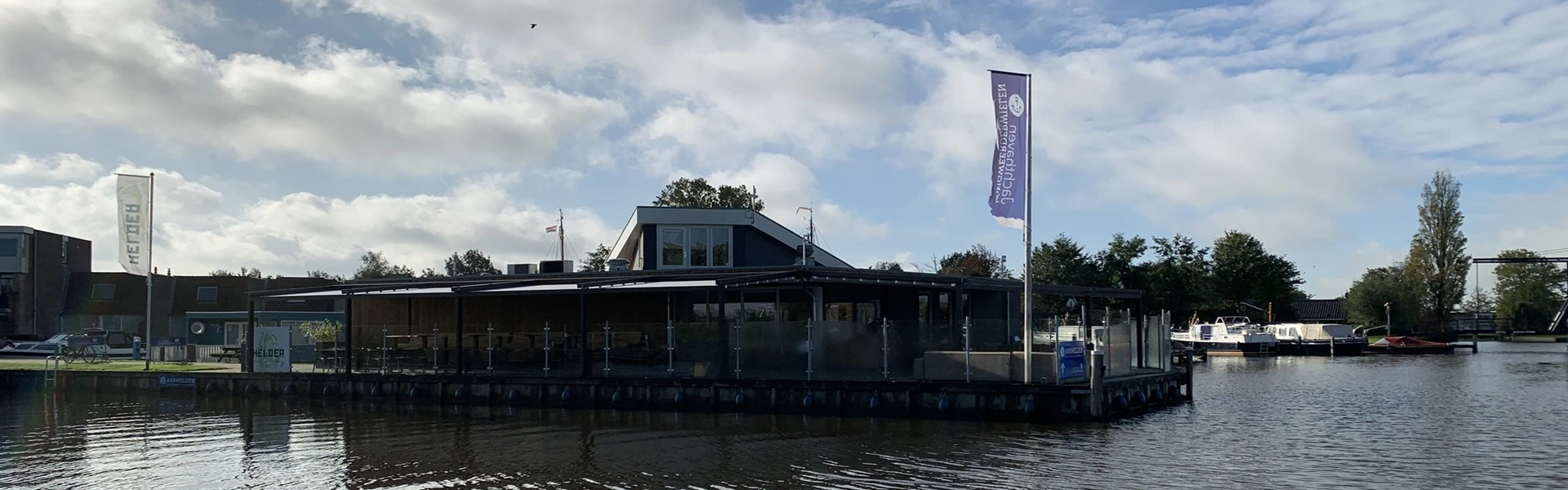 Overkapping met schuifdak bij horecalocatie en uitzicht op een haven