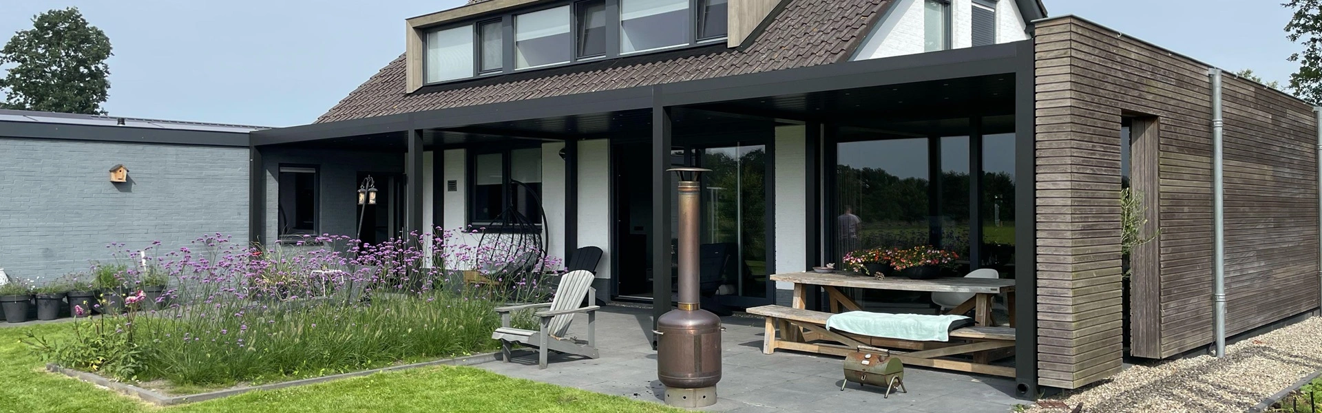 Overkapping met zwarte frame en tuintafel naast houten gevel