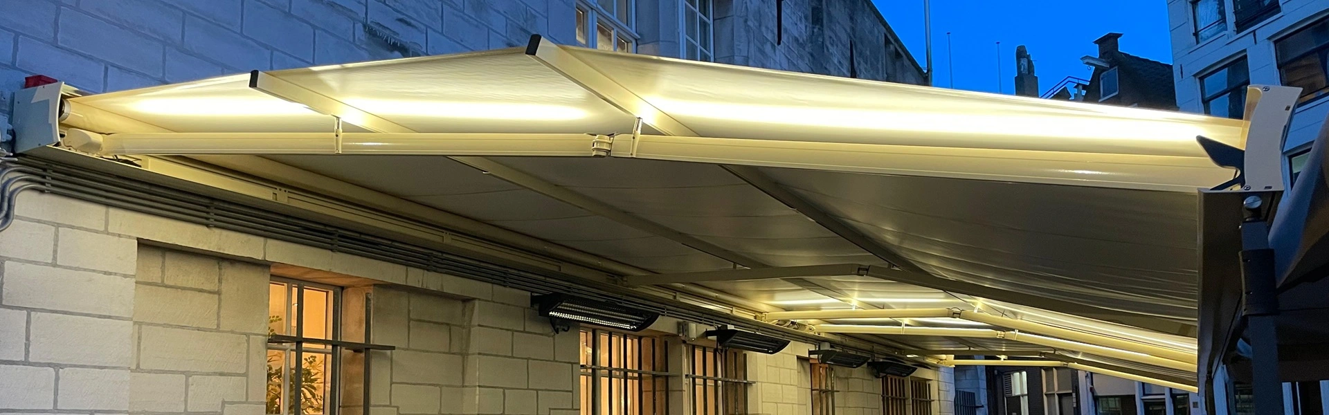 Verlichte terrasoverkapping met heaters aan een gevel