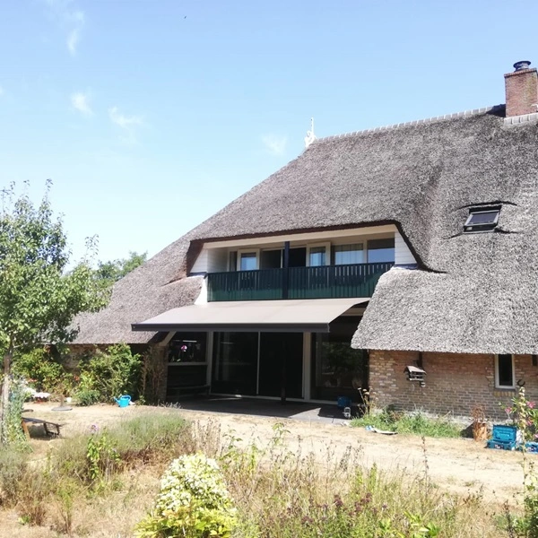 Zon en regenscherm boven terras bij rietgedekte woning voor beschutting