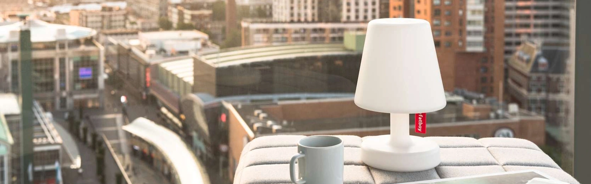 Fatboy tafellamp op een vensterbank met uitzicht over een stedelijk landschap