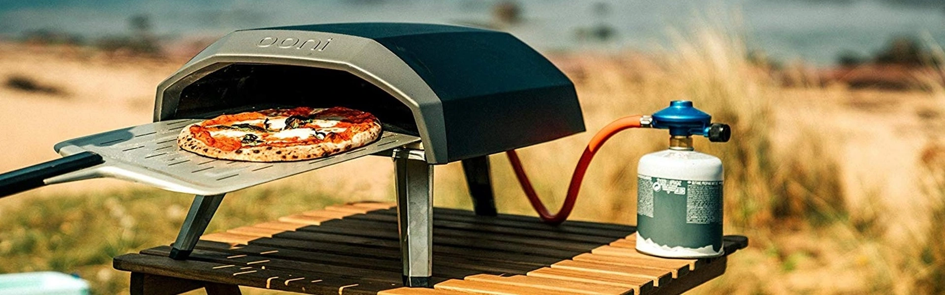 Gasgestookte Ooni pizza oven met pizza en gasfles op houten tafel