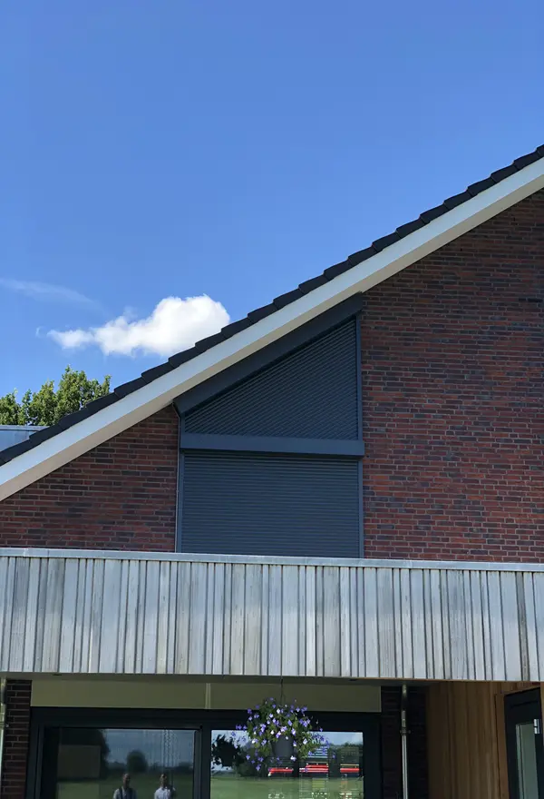 Gesloten rolluiken op schuine gevel van woning met houten afwerking Gesloten rolluiken op schuine gevel van woning met houten afwerking