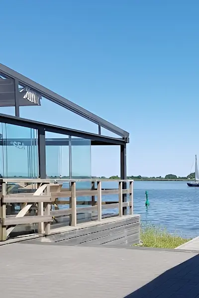 Glazen schuifwanden bij een terras aan het water met uitzicht op een zeilboot Glazen schuifwanden bij een terras aan het water met uitzicht op een zeilboot