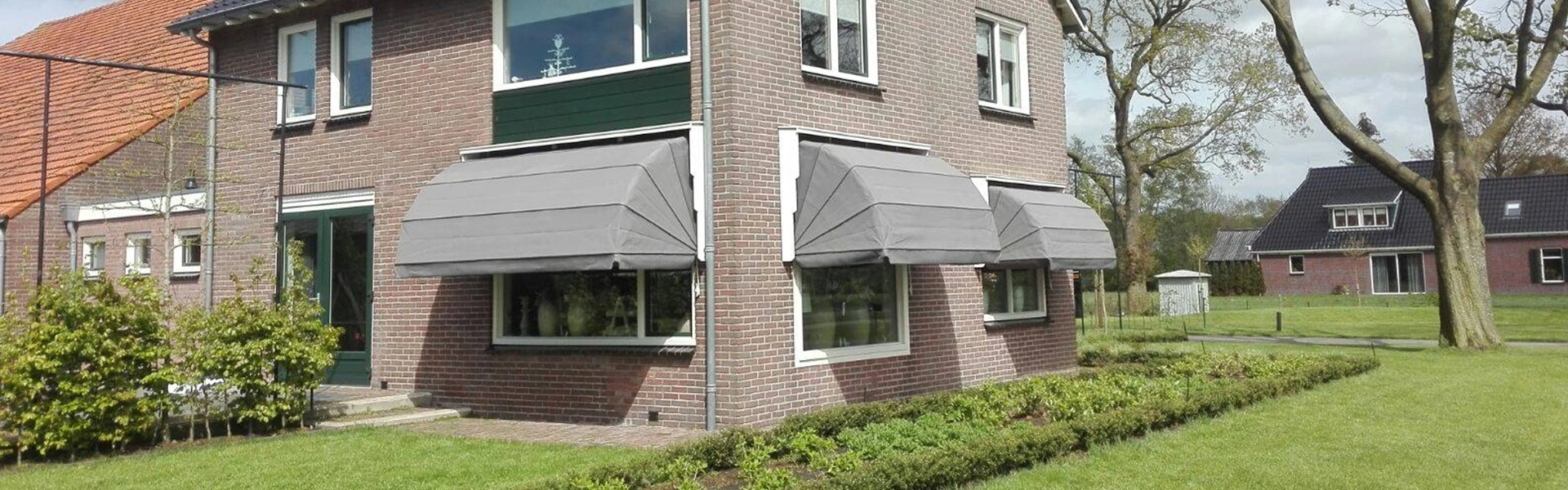 Grijze markiezen op de zijgevel van een bakstenen woning met groene omlijsting (1)