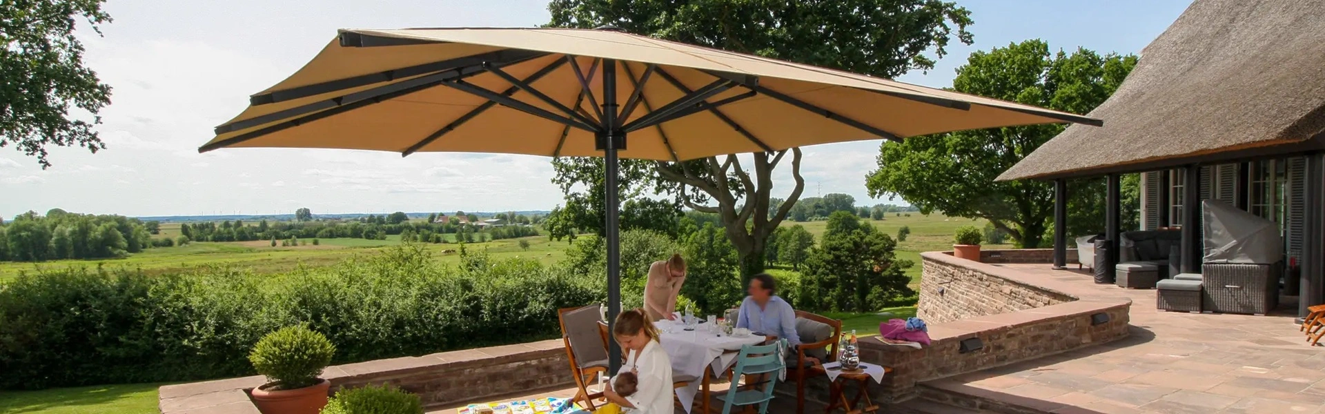 Grote parasol op een ruim terras met uitzicht op groene weilanden