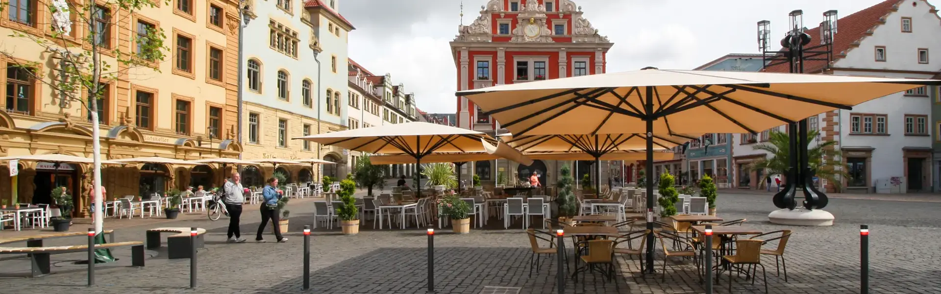 Grote parasols Albatros voor een wit modern gebouw met terrasstoelen