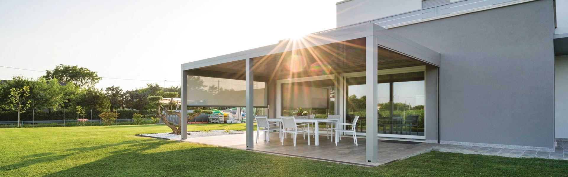 Lamellen overkapping Joy met zonnestralen, glazen schuifdeuren en tuin
