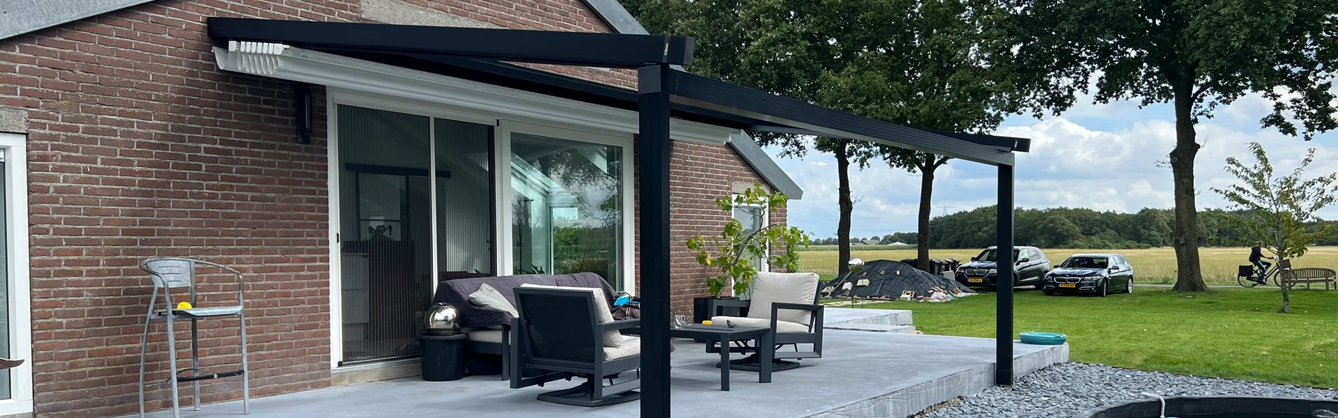 Landelijke tuin met aluminium overkapping en terras bij een stenen woning