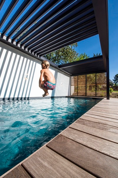 Renson Camargue Skye met intrekbare lamellen boven zwembad en houten terras Renson Camargue Skye met intrekbare lamellen boven zwembad en houten terras