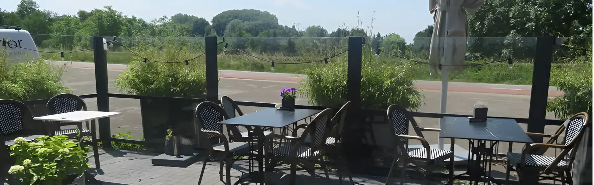 Windscherm Belles met glazen panelen en terrasmeubilair in een groene omgeving