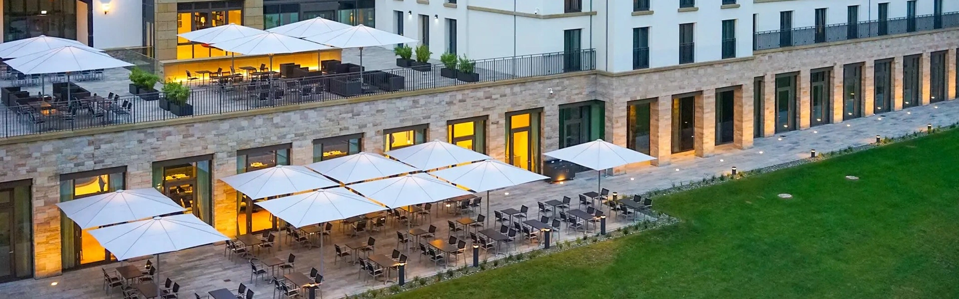 Witte parasols Schatello op een hotelterras met uitzicht op een groen gazon