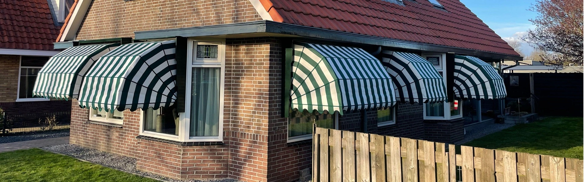 Zijaanzicht van een huis met meerdere houten markiezen in groen-witte strepen