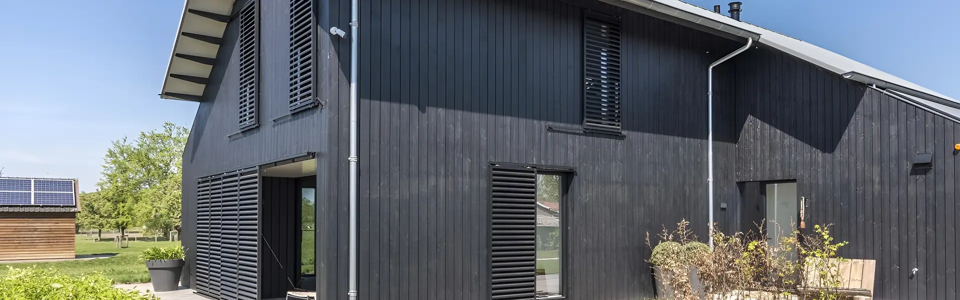 Zwarte houten schuifluiken bij een moderne woning met glazen schuifdeuren