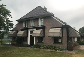Beige markiezen op een landelijke woning met donkere kozijnen