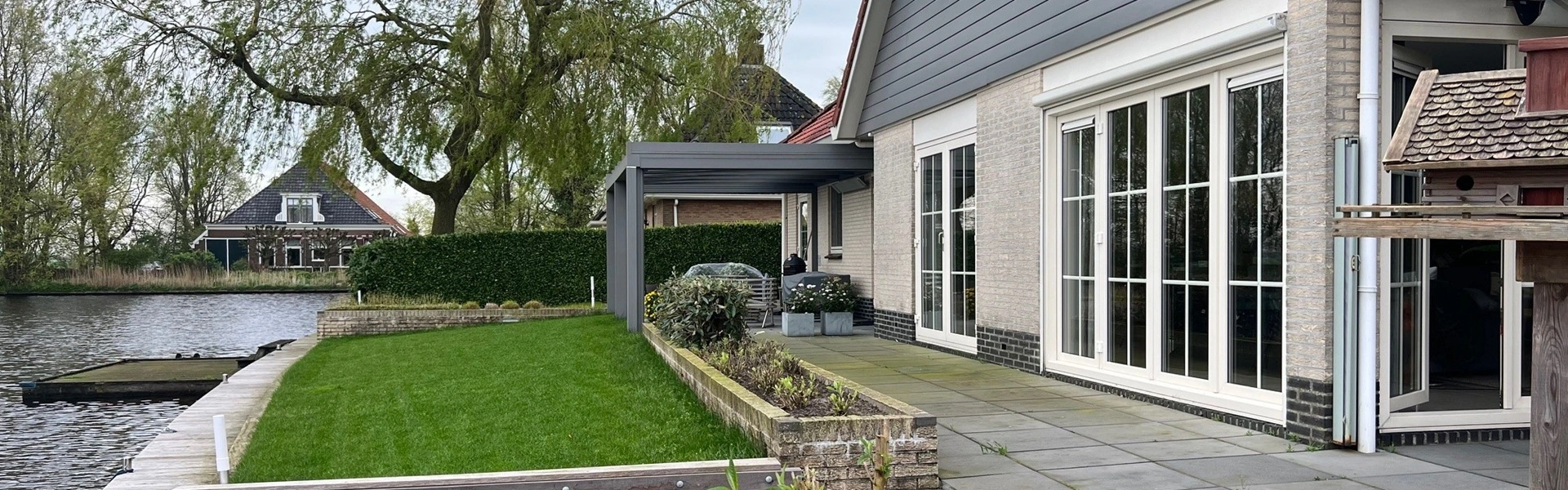 Glazen overkapping met tuin aan het water in Nes gerealiseerd door Veldman Zonwering