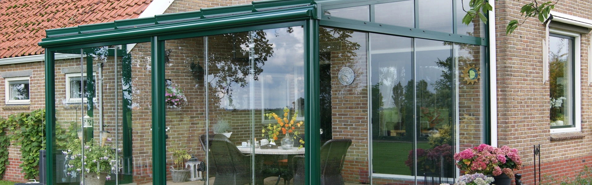 Glazen tuinkamer met groene profielen, geplaatst door Veldman Zonwering aan een landelijke woning