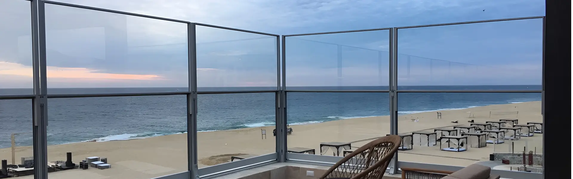 Glazen windschermen op terras in Griekenland met uitzicht op zee en strandbedden.