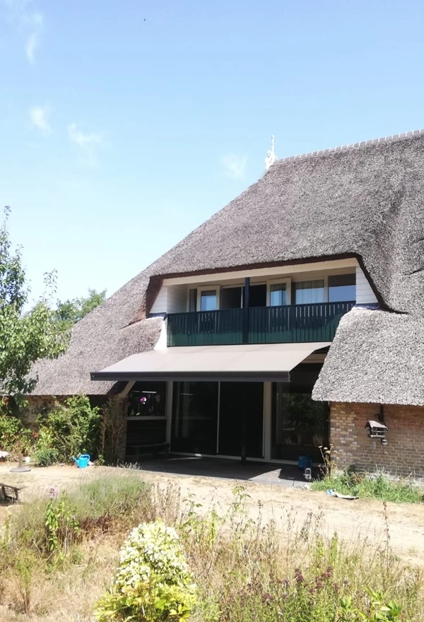Rietgedekt huis met zon- en regenscherm in Reis door Veldman Zonwering
