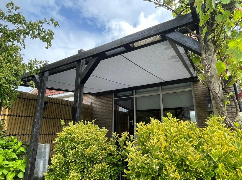 Serrezonwering met zwart houten frame en strak doek in groene tuin Serrezonwering met zwart houten frame en strak doek in groene tuin