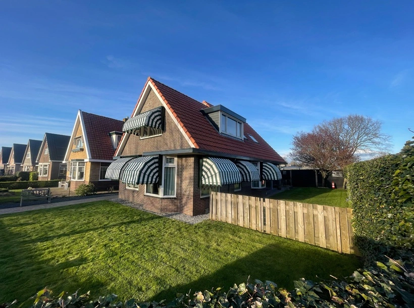 Vrijstaande woning met groen-wit gestreepte markiezen en een rode dakbedekking