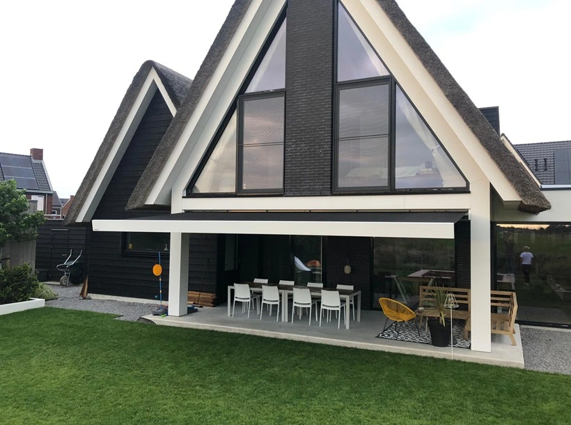 Woning met rieten dak en knikarmscherm boven terras met eettafel en zitgedeelte