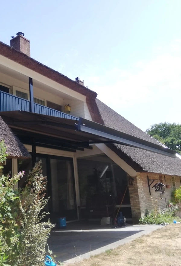 Zon- en regenscherm aan rietgedekt huis in Reis door Veldman Zonwering